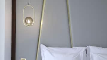 A neatly made bed with white linens and a brown throw blanket, a bedside table with a glass, and a modern pendant light fixture.