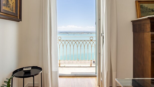 Una stanza con vista sul mare, da un balcone con ringhiera in metallo.
