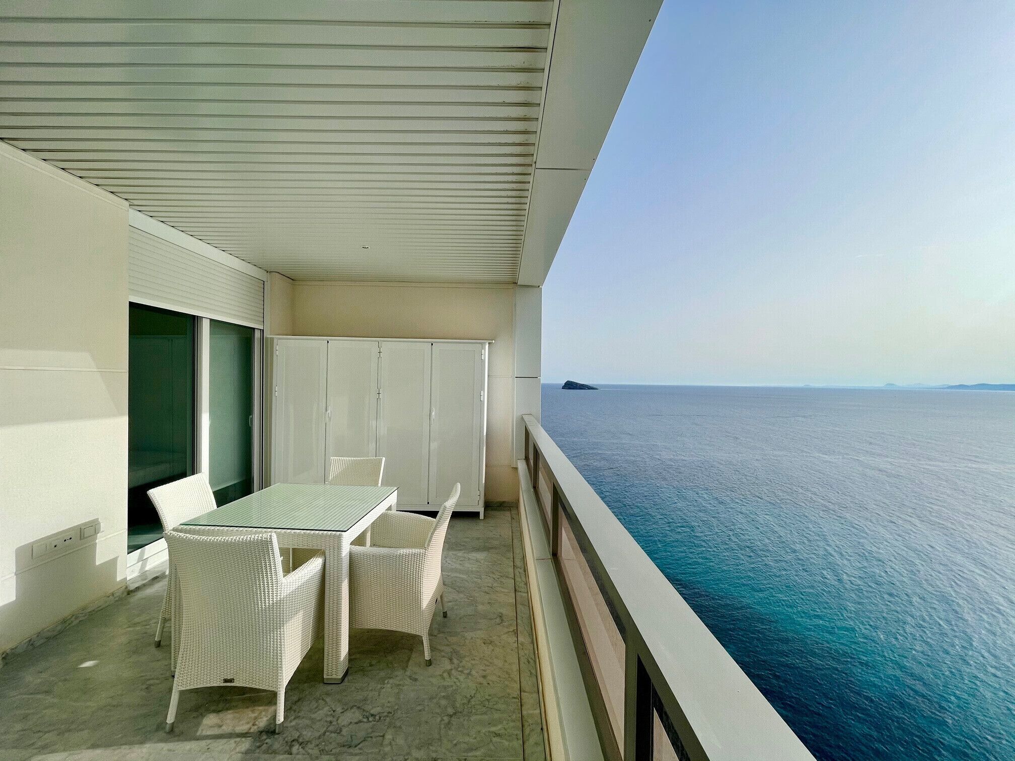 Ein Balkon mit Tisch und Stühlen mit Blick auf ein ruhiges Meer.