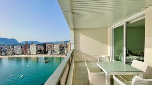 A balcony with a view of a beach and cityscape, featuring a glass table and wicker chairs. - MEDITERRANEAN VIEW BENIDORM R078 (Benidorm)