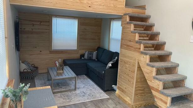 A compact living space with a built-in sofa, a coffee table, a small rug, and a wooden staircase. - Cozy Tiny Home in Heart of Big Sandy (Big Sandy)
