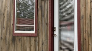 A wooden building with two windows and a door, each with a white frame and a small light fixture above the left window. - Cozy Tiny Home in Heart of Big Sandy (Big Sandy)