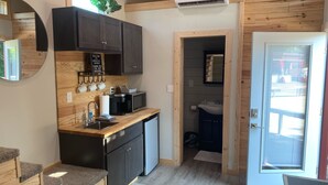 A compact kitchen with dark cabinets, a coffee machine, and a microwave. There is a sink, a small refrigerator, and a welcome sign above the cabinets. - Cozy Tiny Home in Heart of Big Sandy (Big Sandy)