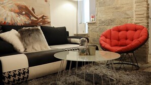 Un salon moderne avec un canapé noir et blanc, un fauteuil rouge, une petite table ronde et une lampe.