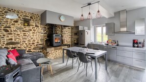 Una cocina moderna con pared de piedra, una zona de comedor con sillas y un sofá gris con cojines rojos.