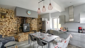 Cocina moderna con pared de piedra, armarios grises y comedor con mesa dispuesta para cuatro.
