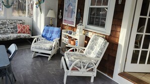 Una habitación acogedora con un sofá blanco, dos sillas de mimbre, una mesita y una ventana con un cartel.