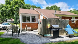 Un patio trasero con un porche, mobiliario exterior, una parrilla y una valla de madera.