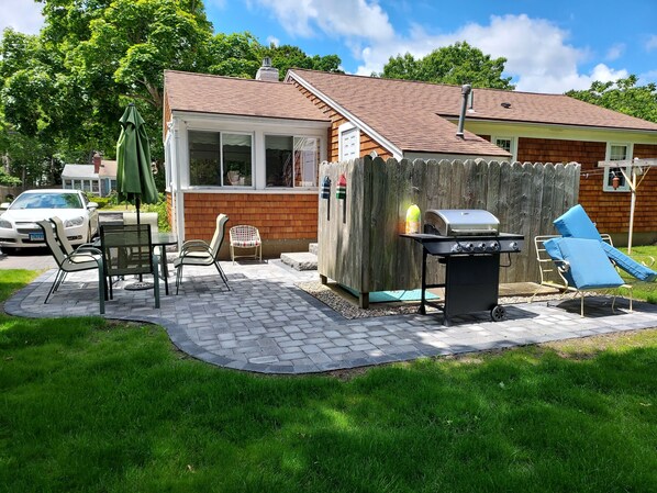 A backyard with a patio, outdoor seating, a grill, and a wooden fence.