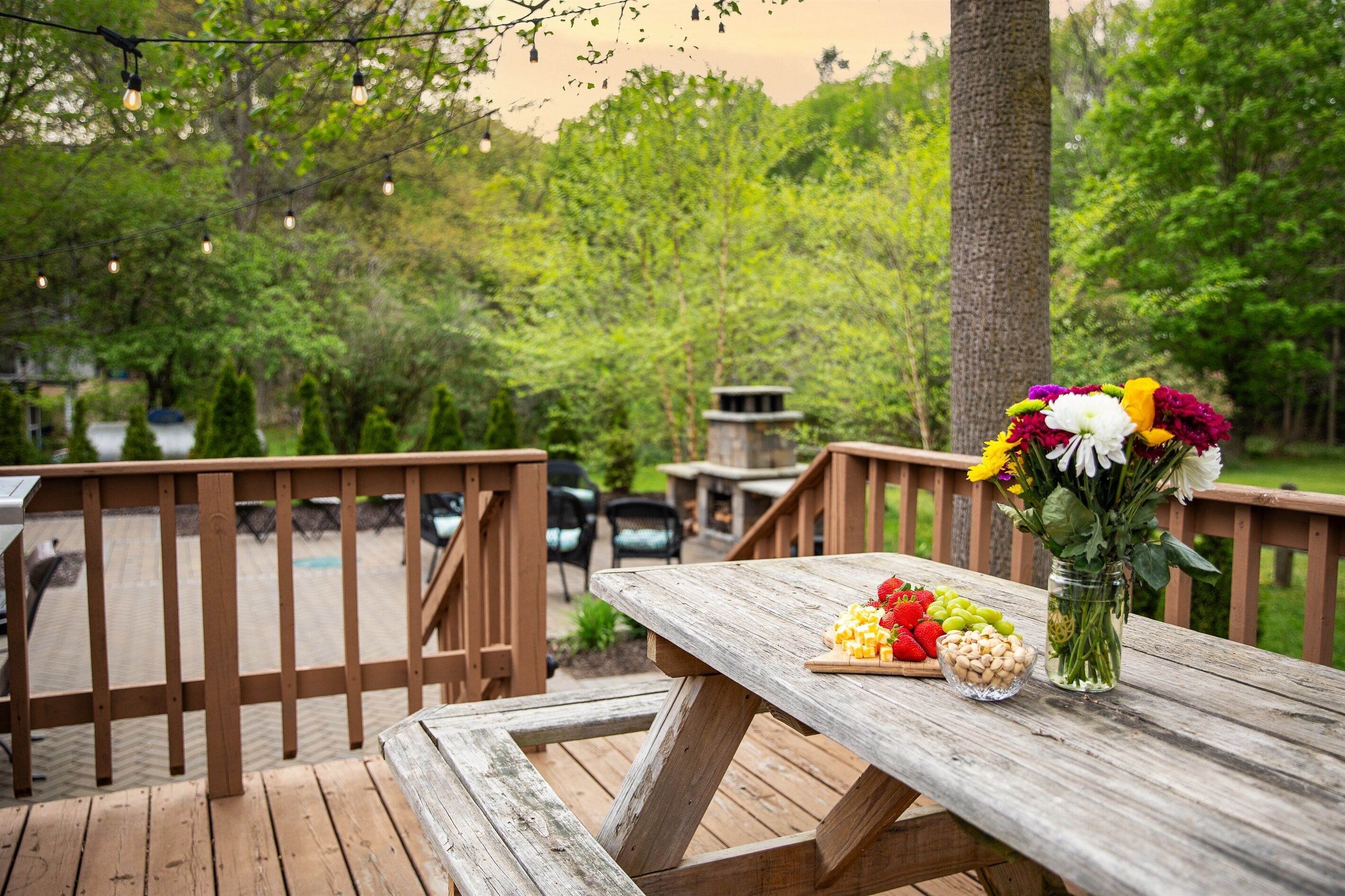A wooden deck with a picnic table, a vase of flowers, and a bowl of fruit.