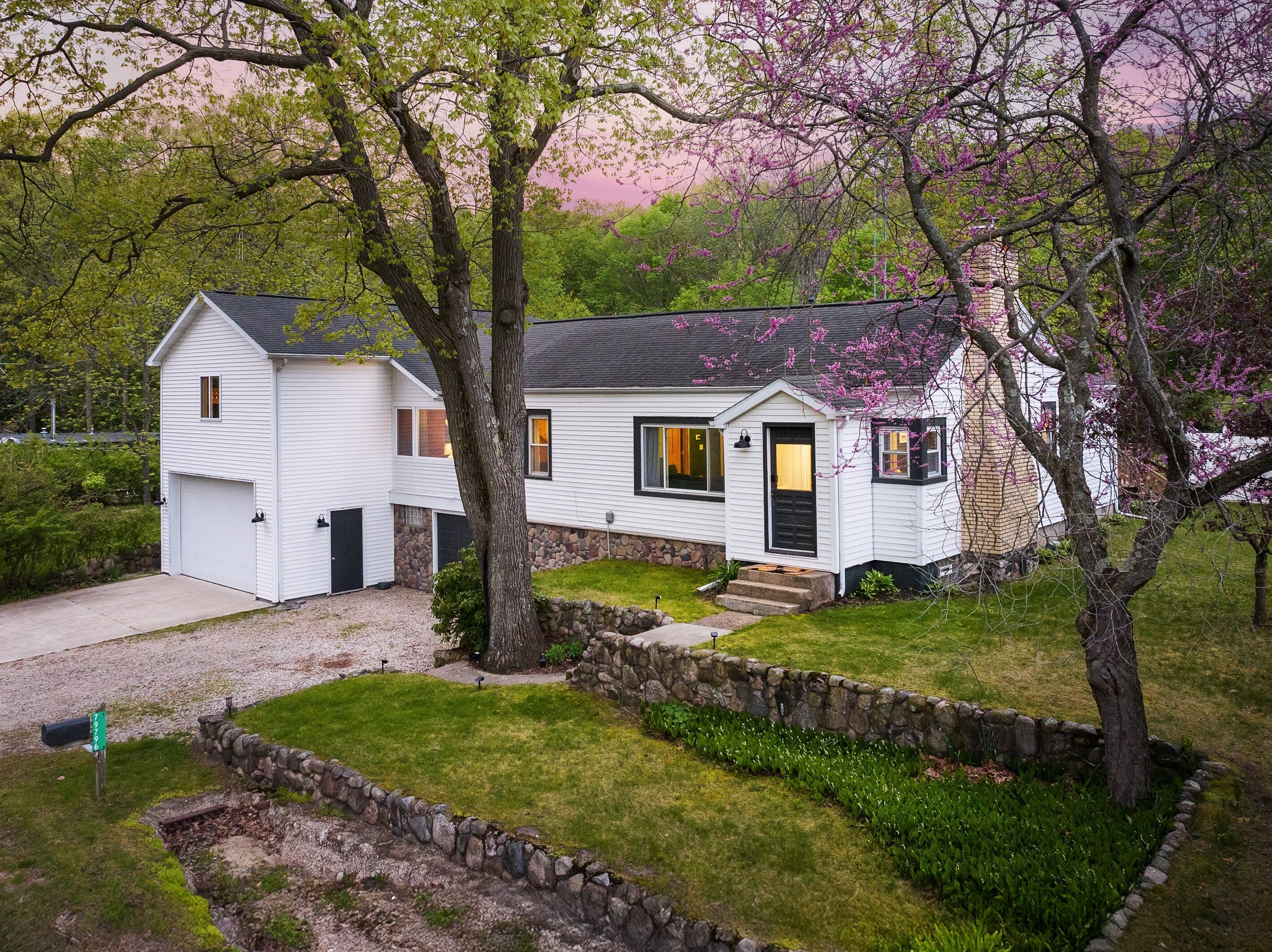 A two-story house with a garage, a stone wall, and a well-maintained lawn.