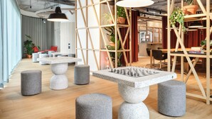 Un espacio de oficina moderno con una gran mesa de ajedrez, varias zonas de estar y estanterías de madera con plantas.