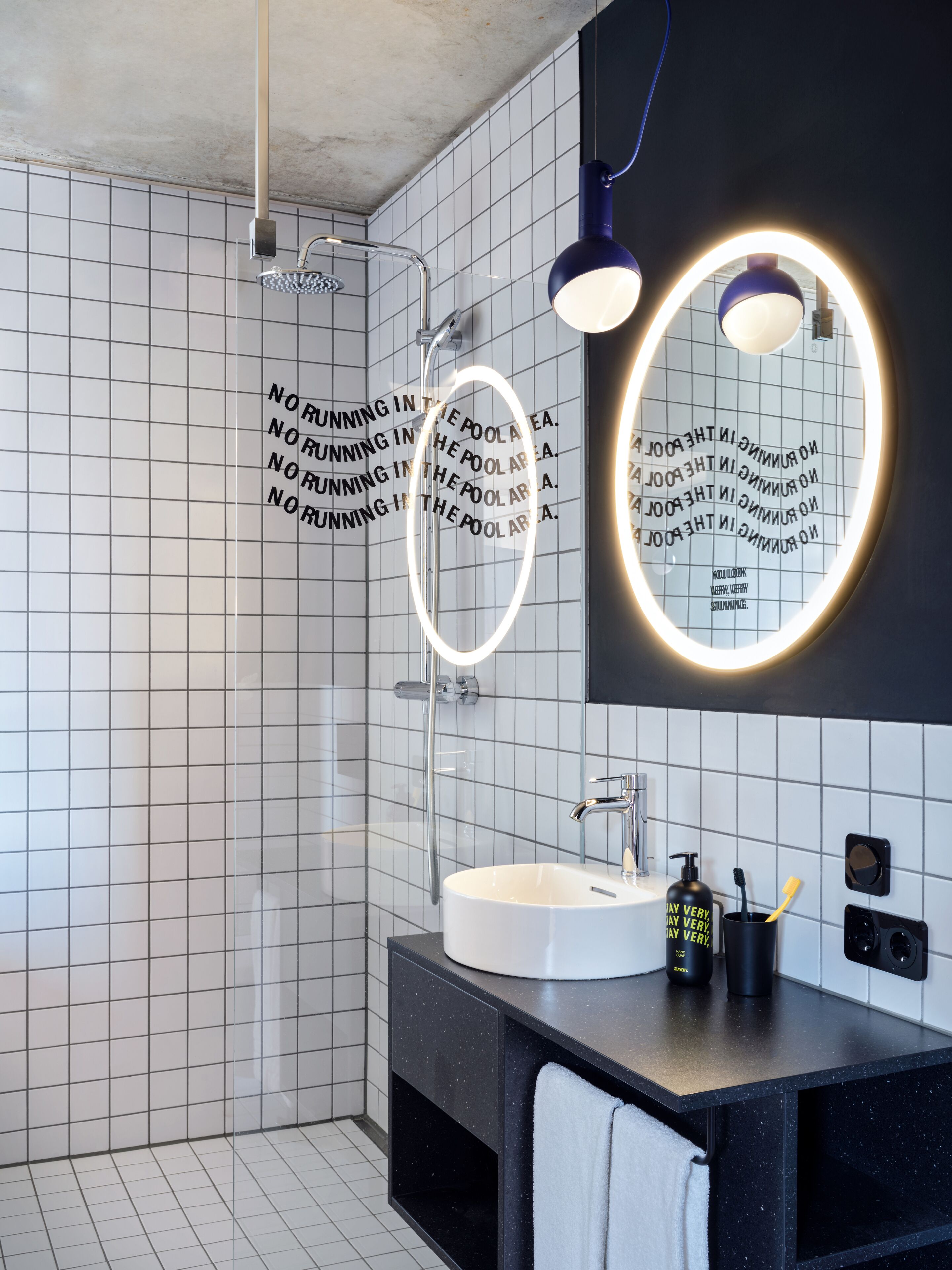 A modern bathroom with a white sink, black countertop, and a mirror with a circular light.