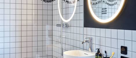 A modern bathroom with a white sink, black countertop, and a mirror with a circular light.