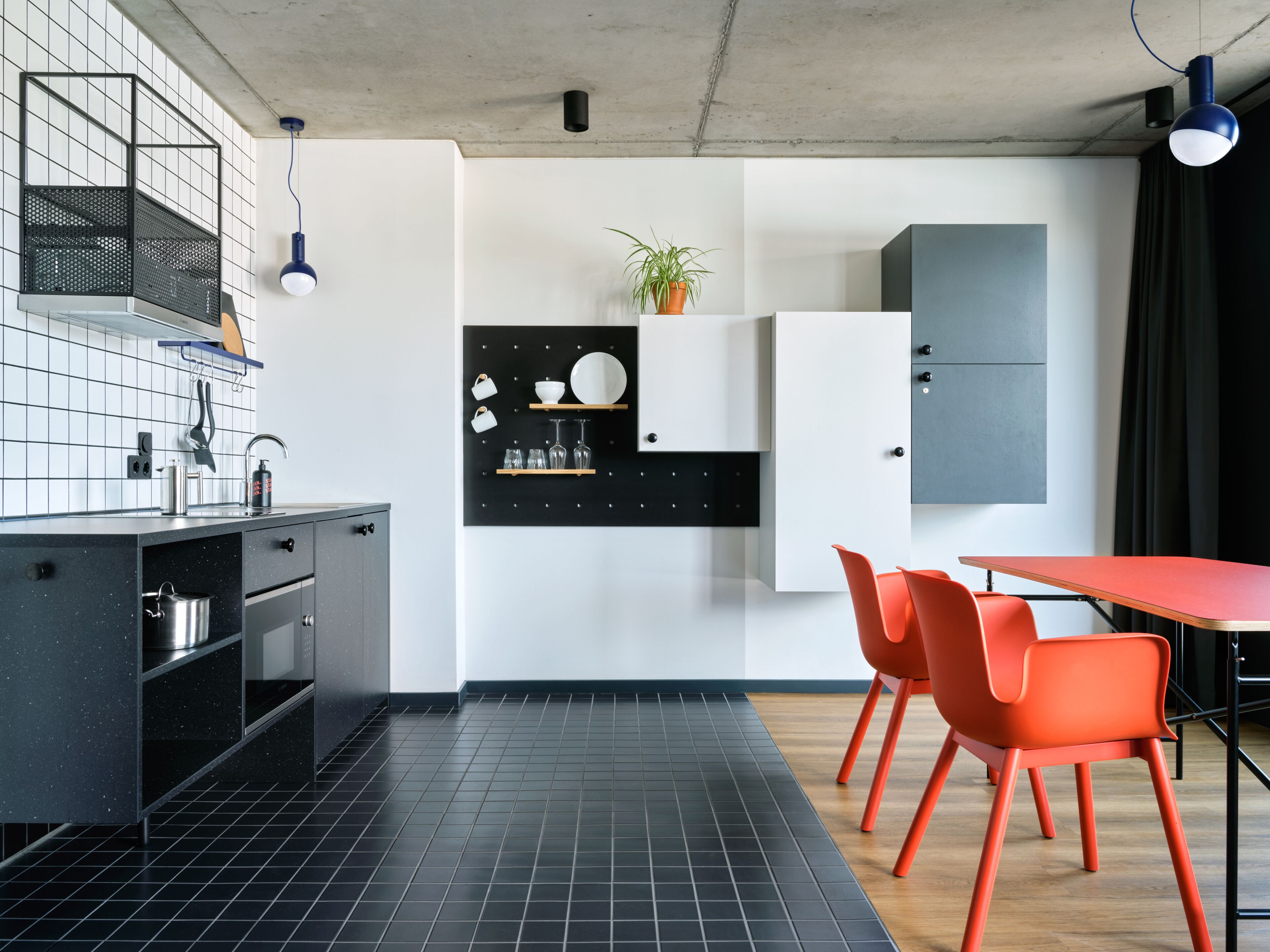 A modern kitchen with black cabinets, a white countertop, and a dining area with orange chairs.