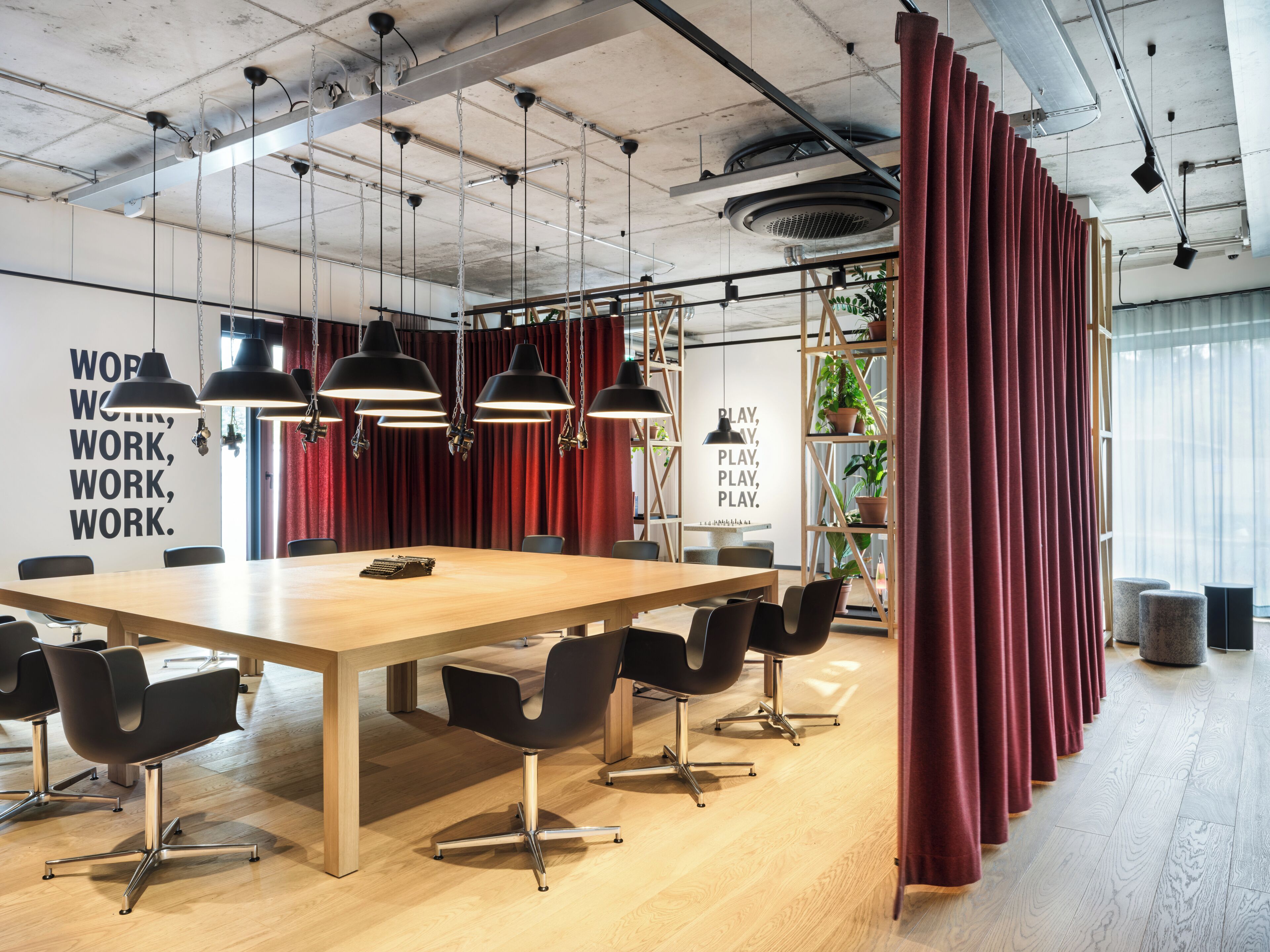Une salle de conférence moderne, dotée d’une longue table, de chaises noires, de luminaires suspendus et de rideaux rouges.