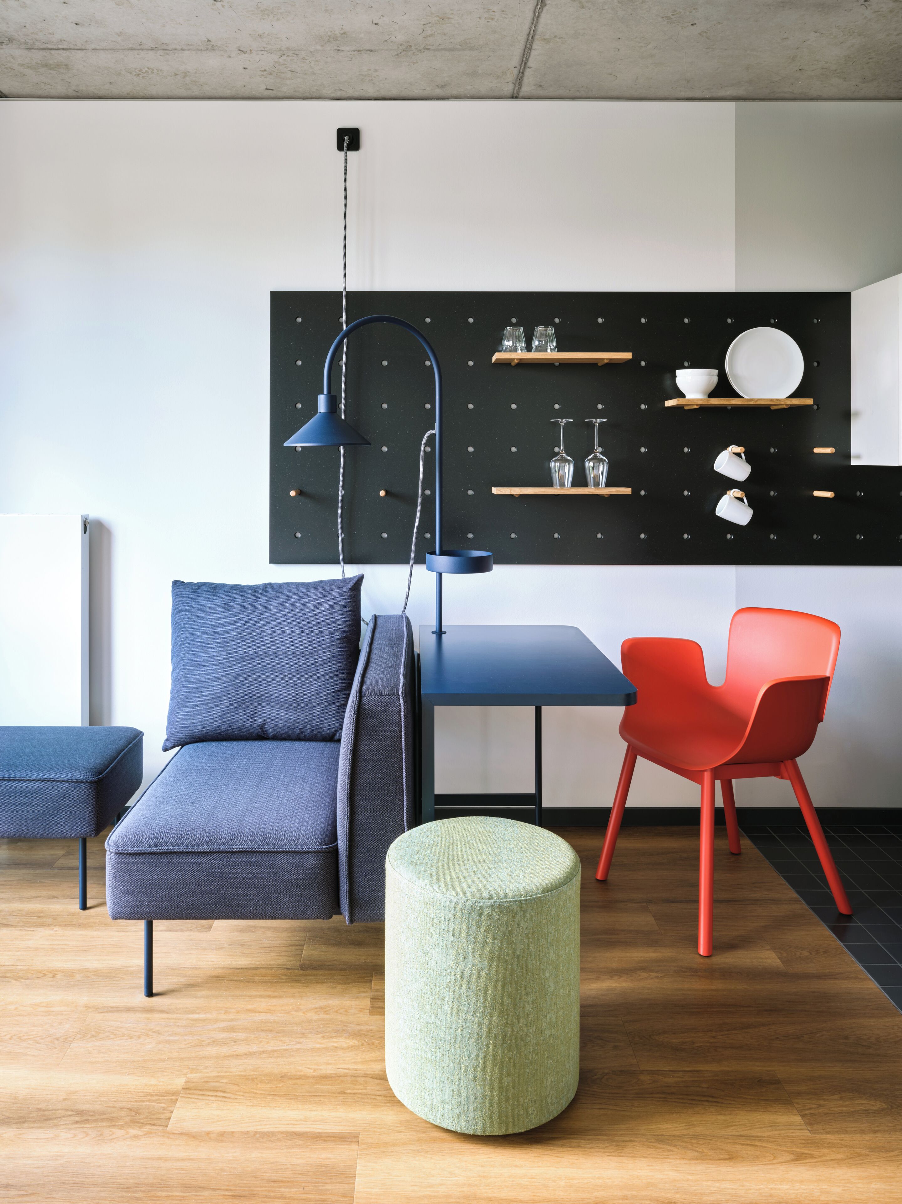 A modern living room with a grey sofa, a red chair, a blue table, and a green ottoman.