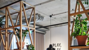 Una habitación moderna con estanterías de madera, plantas en macetas, una mesa de fútbol de mesa y una pared con el texto “PLAY, PLAY, PLAY”.