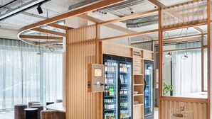 Un interior moderno con separaciones de madera, una zona de estar con taburetes redondos y un refrigerador de bebidas con la etiqueta 'COLD DRINKS, WARM FEELINGS'.