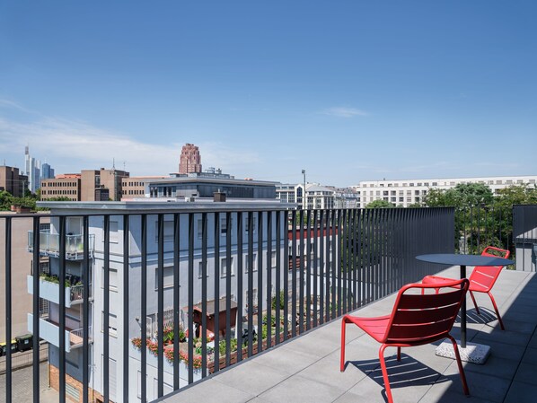 A rooftop terrace with red chairs and a table, overlooking a cityscape with modern buildings. - STAYERY Frankfurt Sachsenhausen (Frankfurt)