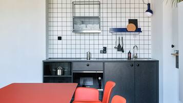 A modern kitchen with a red table and orange chairs, a black countertop, a sink, and a backsplash with a grid pattern.