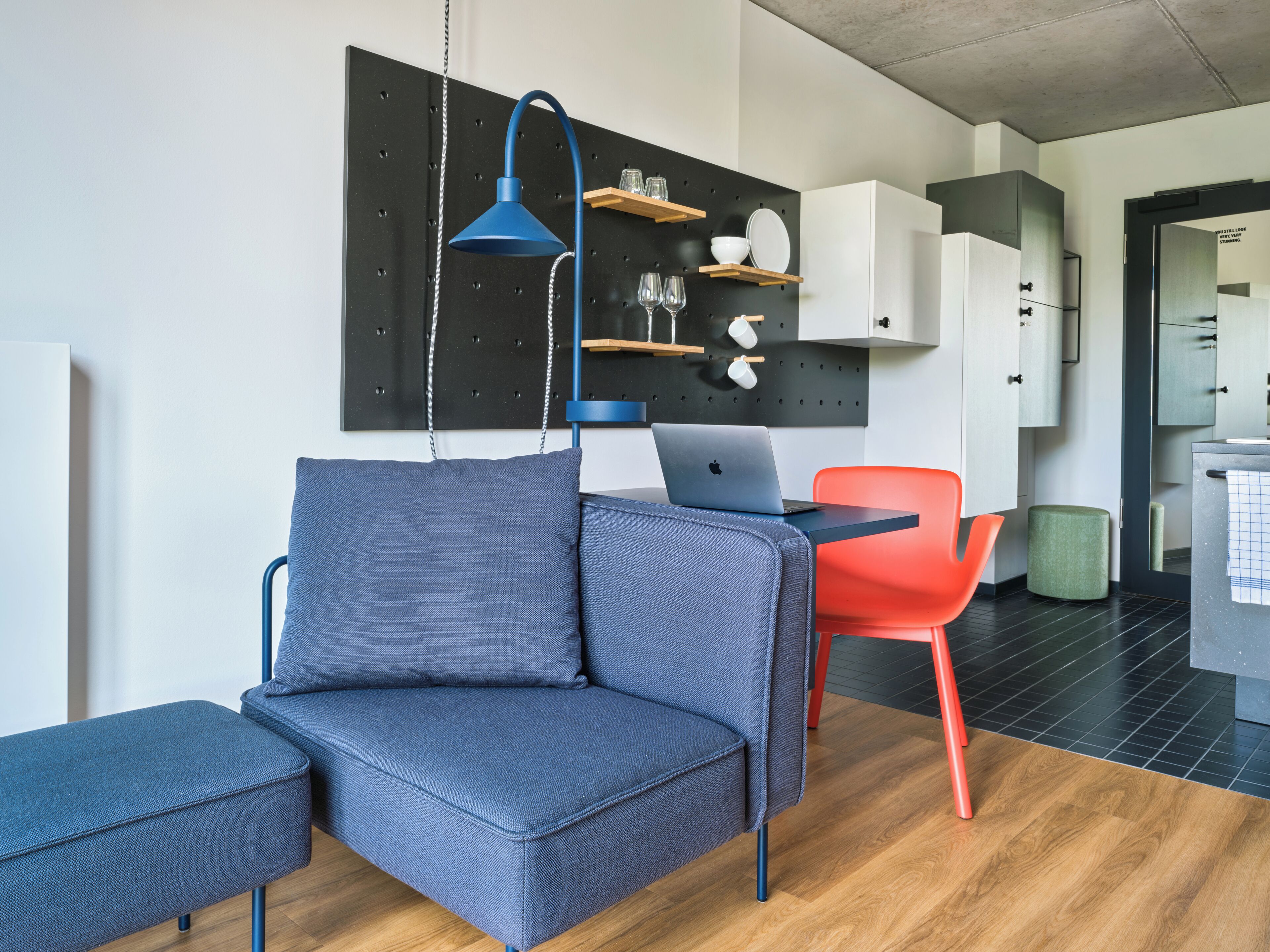 A modern living room with a blue sofa, a red chair, and a laptop on a table.