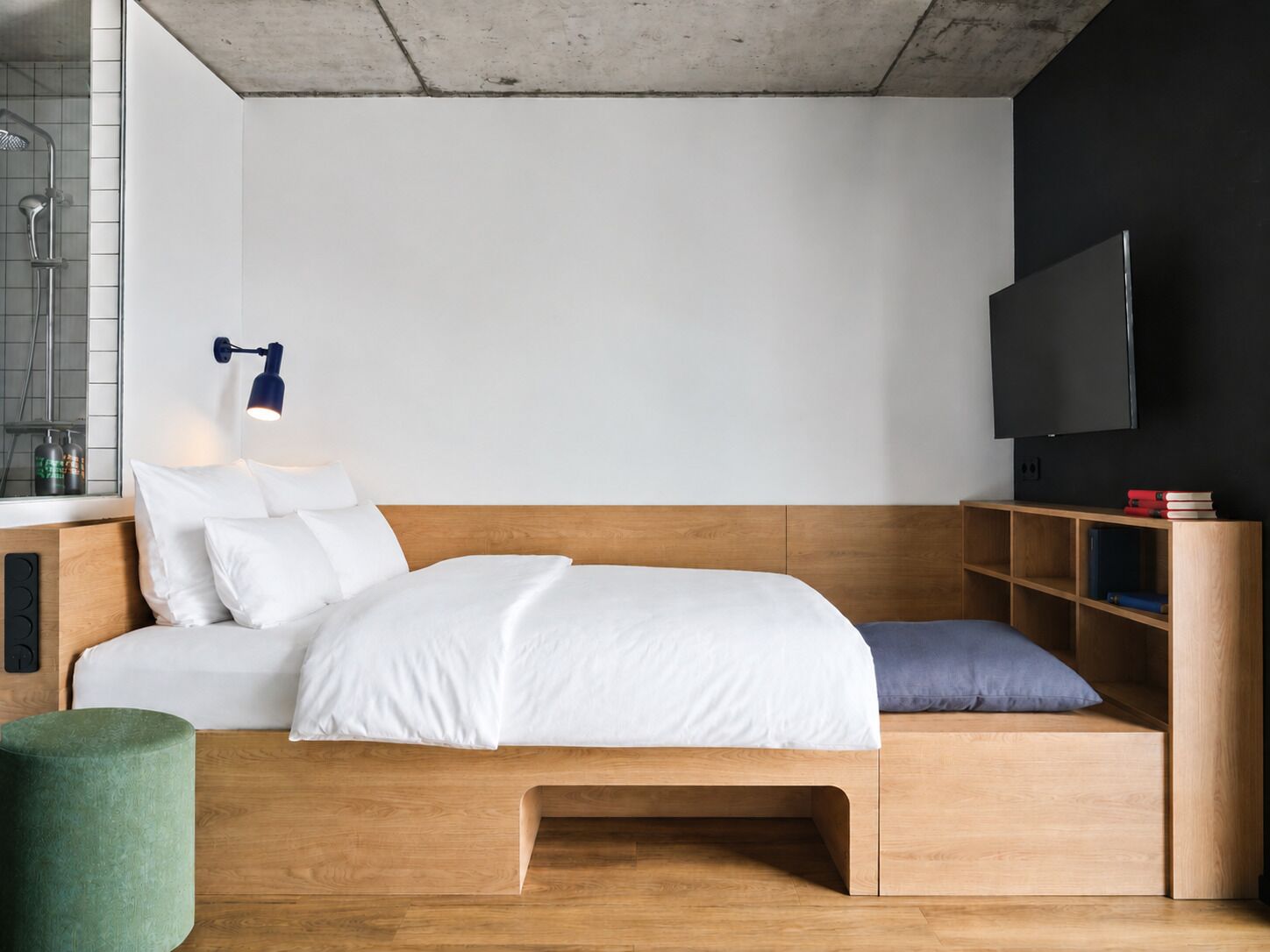 Um quarto moderno com uma cama de madeira, uma mesa de cabeceira com abajur, uma televisão e uma pequena estante com livros.