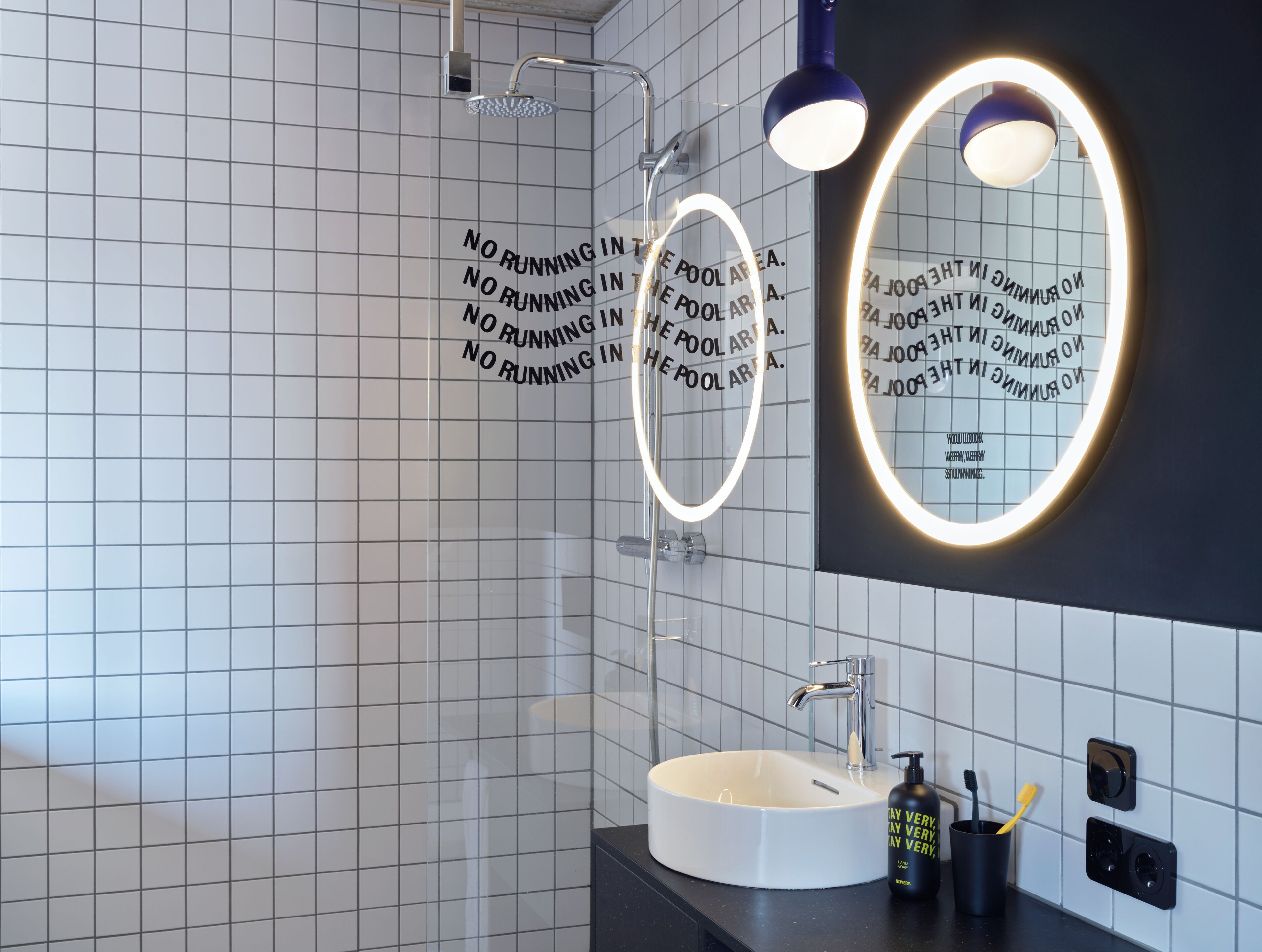 Un baño moderno con un lavamanos blanco, un espejo con iluminación envolvente y una ducha con puerta de vidrio.