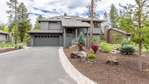 A modern two-story house with a garage, surrounded by a landscaped garden with various plants and rocks. - Maur32-North Sunriver Retreat | Hot Tub, AC, Bikes, Ping Pong (Sunriver)