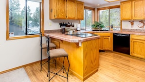 A kitchen with wooden cabinets, a bar stool, a kettle, and a dishwasher. - Maur32-North Sunriver Retreat | Hot Tub, AC, Bikes, Ping Pong (Sunriver)
