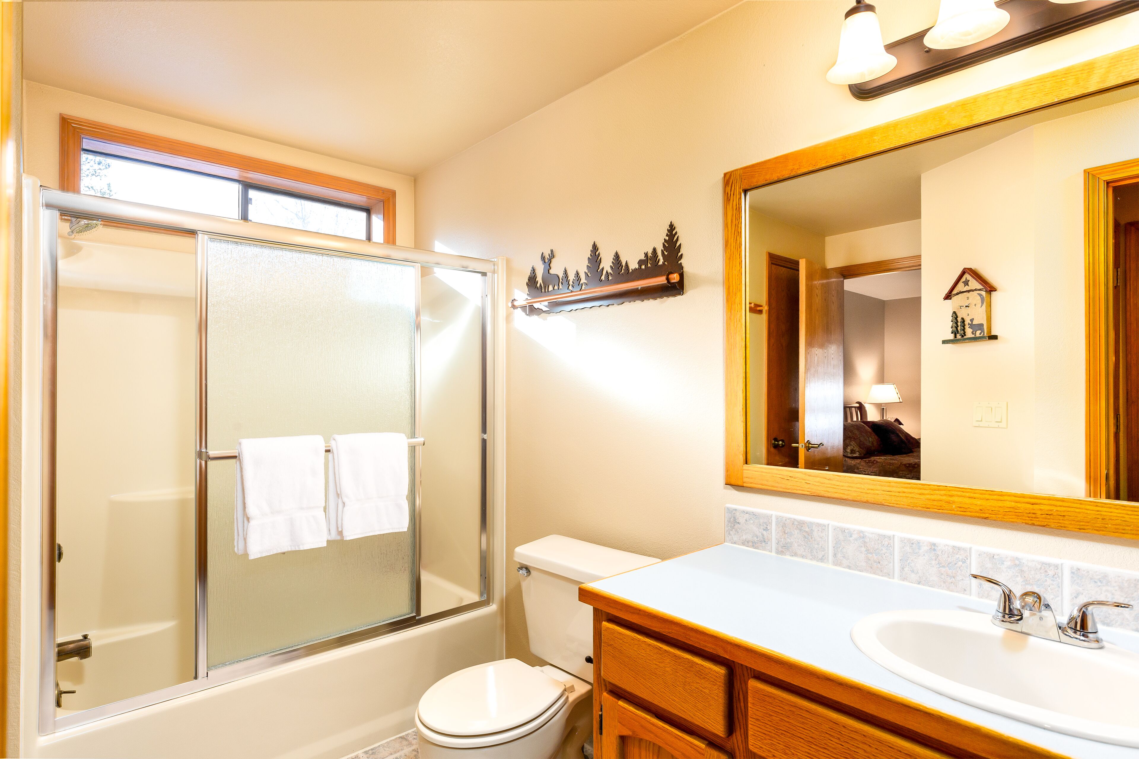 Une salle de bain avec une douche à parois de verre, des toilettes, un lavabo avec un miroir au-dessus et une étagère ornée d’objets décoratifs.