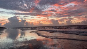 Ein Strand mit einer spiegelnden, nassen Oberfläche und einem Sonnenuntergangshimmel.