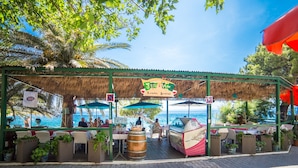 An outdoor dining area with a thatched roof, tables, chairs, and potted plants. - Apt Next to the Beach w Balcony and sea View (Baska Voda)