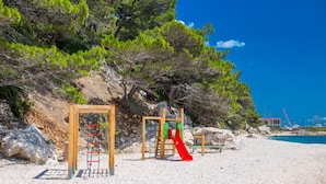 A beach playground with climbing structures and a slide, surrounded by trees and a clear blue sky. - Apt Next to the Beach w Balcony and sea View (Baska Voda)