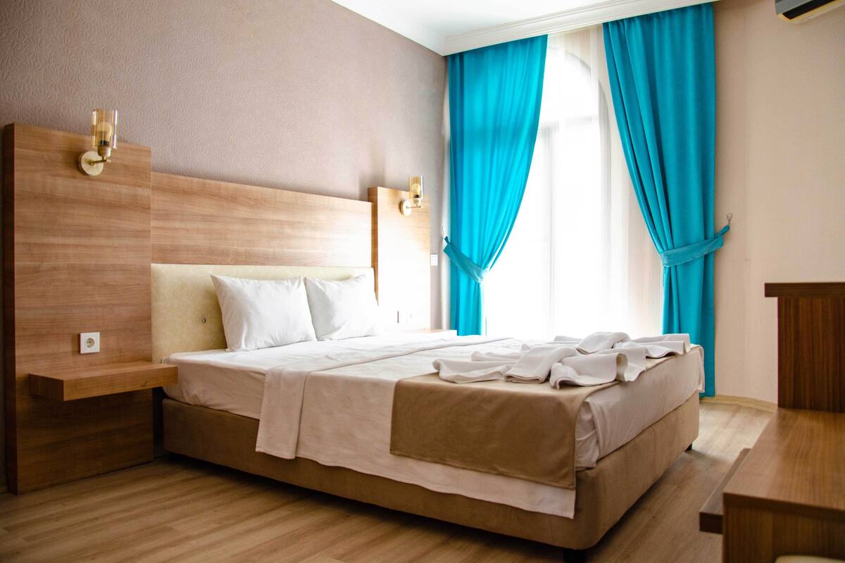 A hotel room with a large bed, wooden headboard, bedside tables, and a window with curtains.