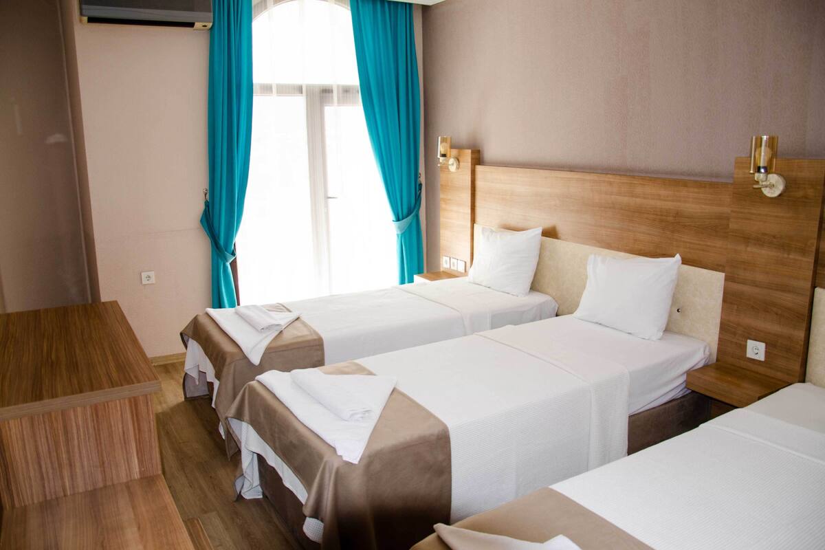 A hotel room with three single beds, wooden headboards, and a small wooden table.
