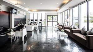 A modern hotel lobby with a black marble floor, white and brown seating, a flat-screen TV, and large windows offering a city view. - Anda Bangkok Hotel (Bangkok)