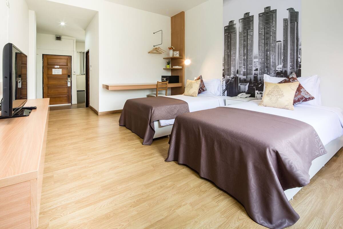 A hotel room with a bed, a desk, a chair, and a cityscape wall art.