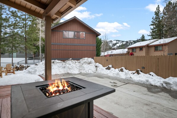 A patio with a fire pit, wooden deck, and a view of a cabin.