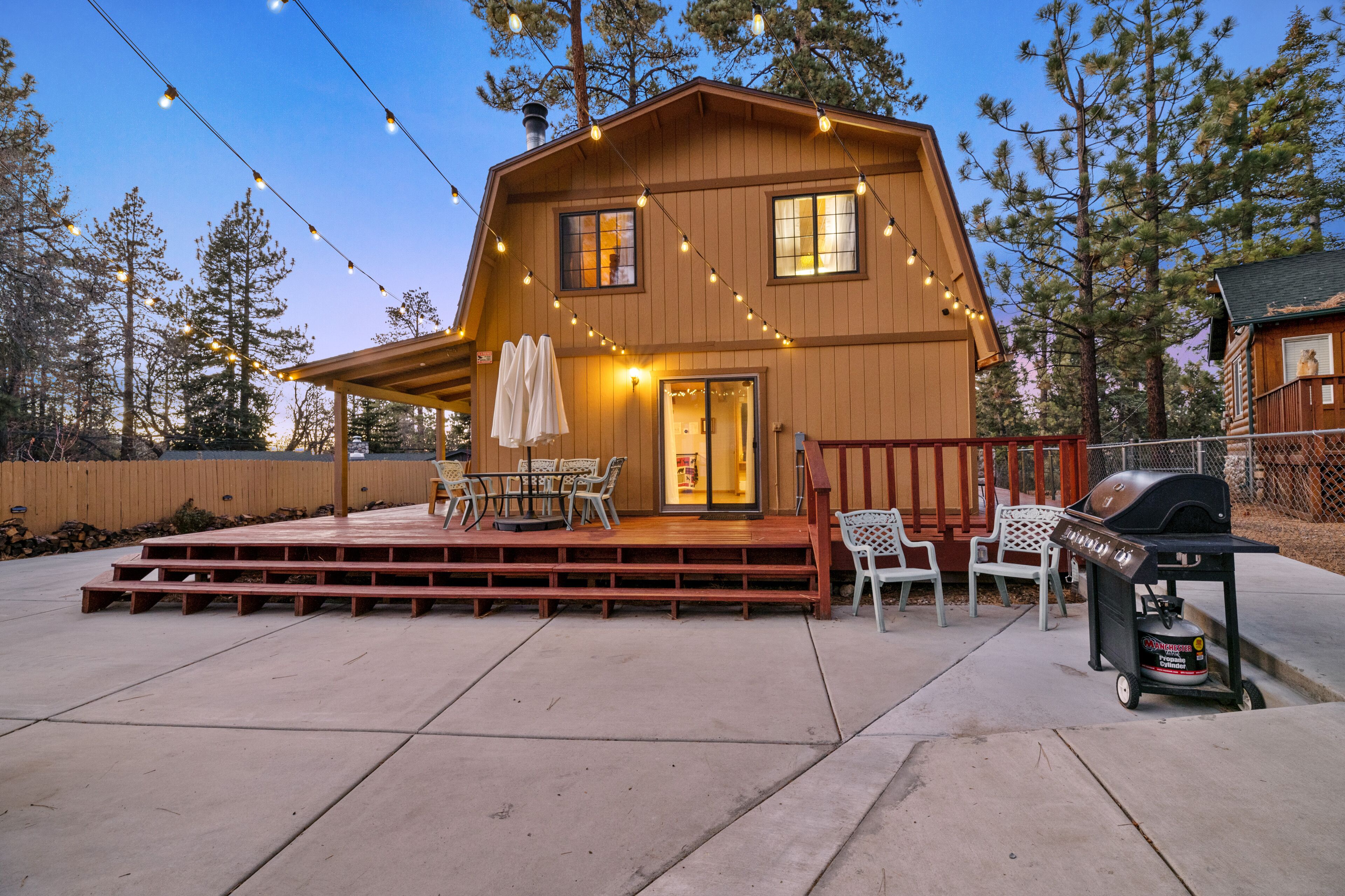 A wooden cabin with a porch, outdoor seating, and a barbecue grill.