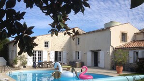 Una piscina con giochi gonfiabili, una zona relax e un edificio in pietra con persiane.