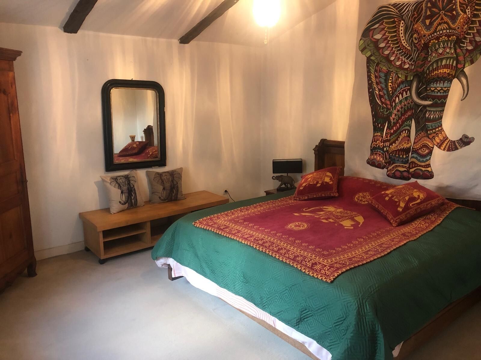 Un dormitorio con cama, un banco, un espejo y un adorno de pared.