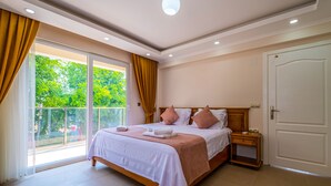 Une chambre avec un grand lit, une table de chevet, une porte et une vue sur la verdure par la fenêtre.