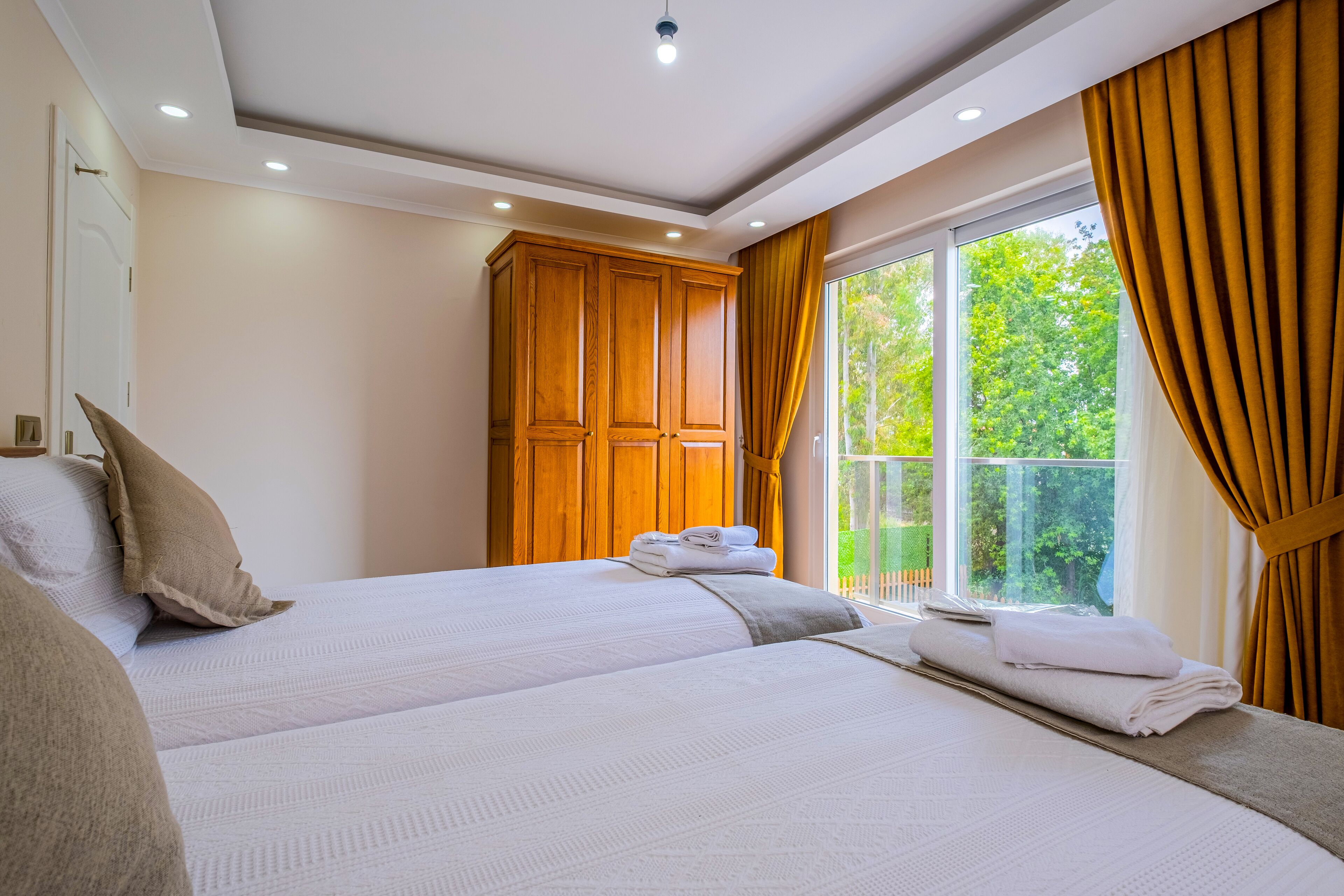 A bedroom with two beds, a wardrobe, and a large window with curtains.