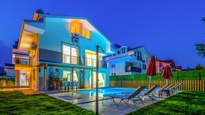 Une maison moderne à deux étages, dotée d’une piscine, d’un espace extérieur aménagé et d’une pelouse bien entretenue.