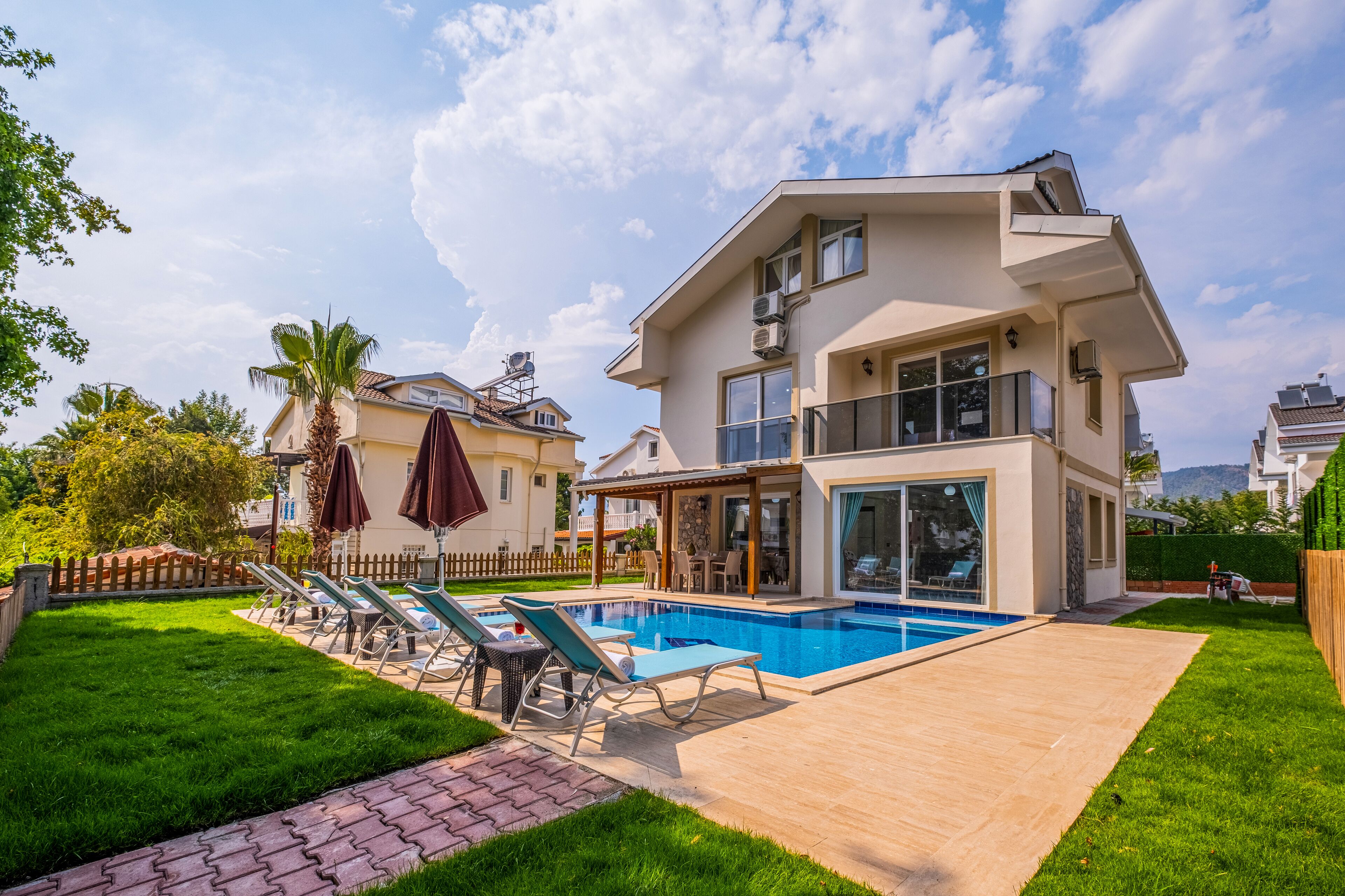 A modern two-story house with a swimming pool, a patio with lounge chairs, and a well-maintained lawn.
