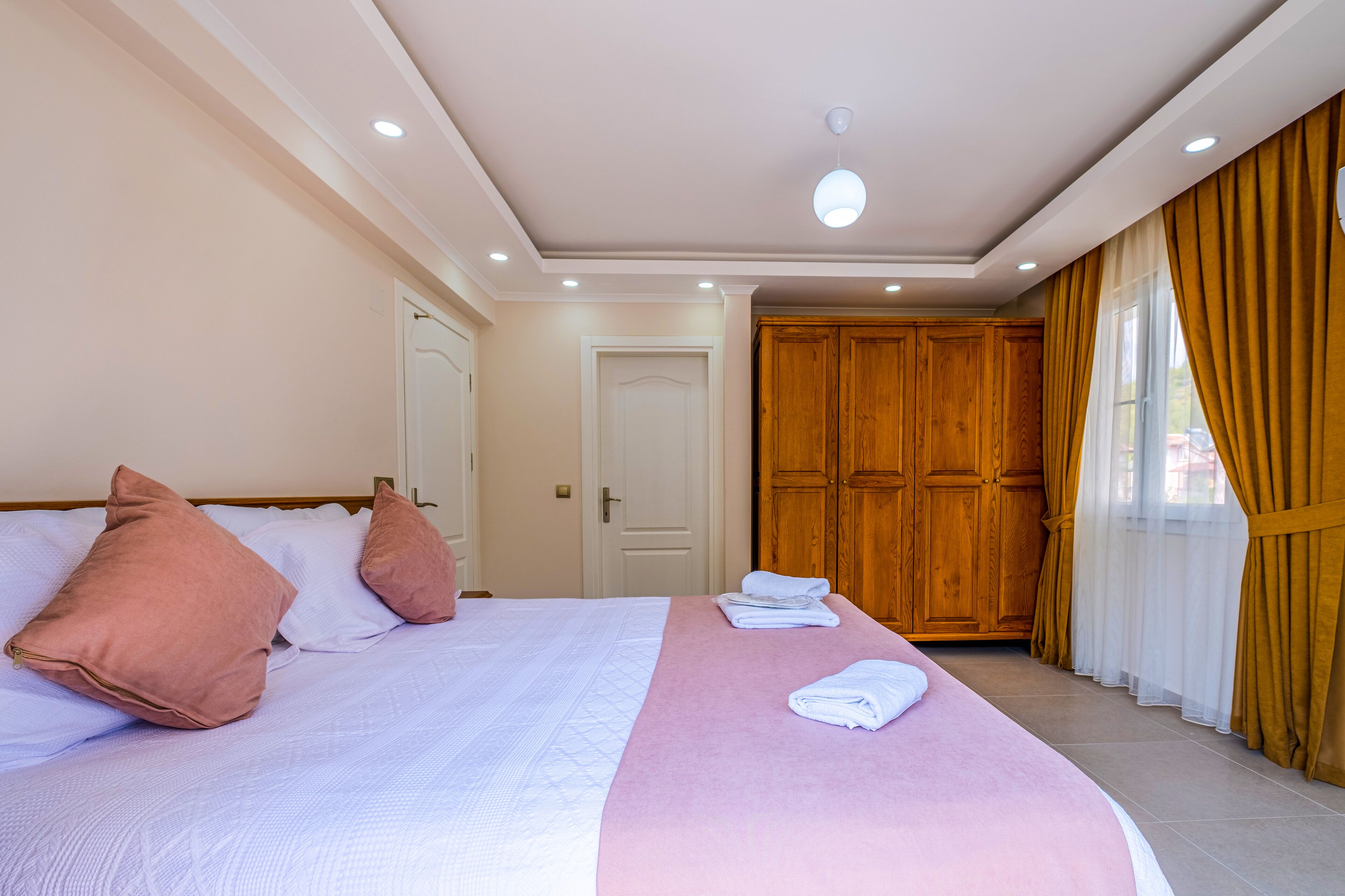 A hotel room with a large bed, wooden wardrobe, and a window with curtains.