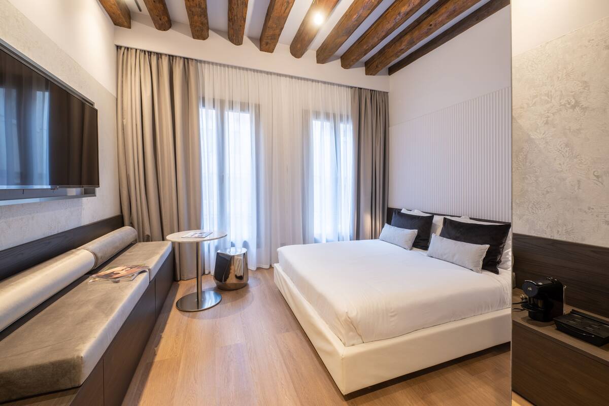 A modern hotel room with a large bed, a seating area, a small table, and a TV.