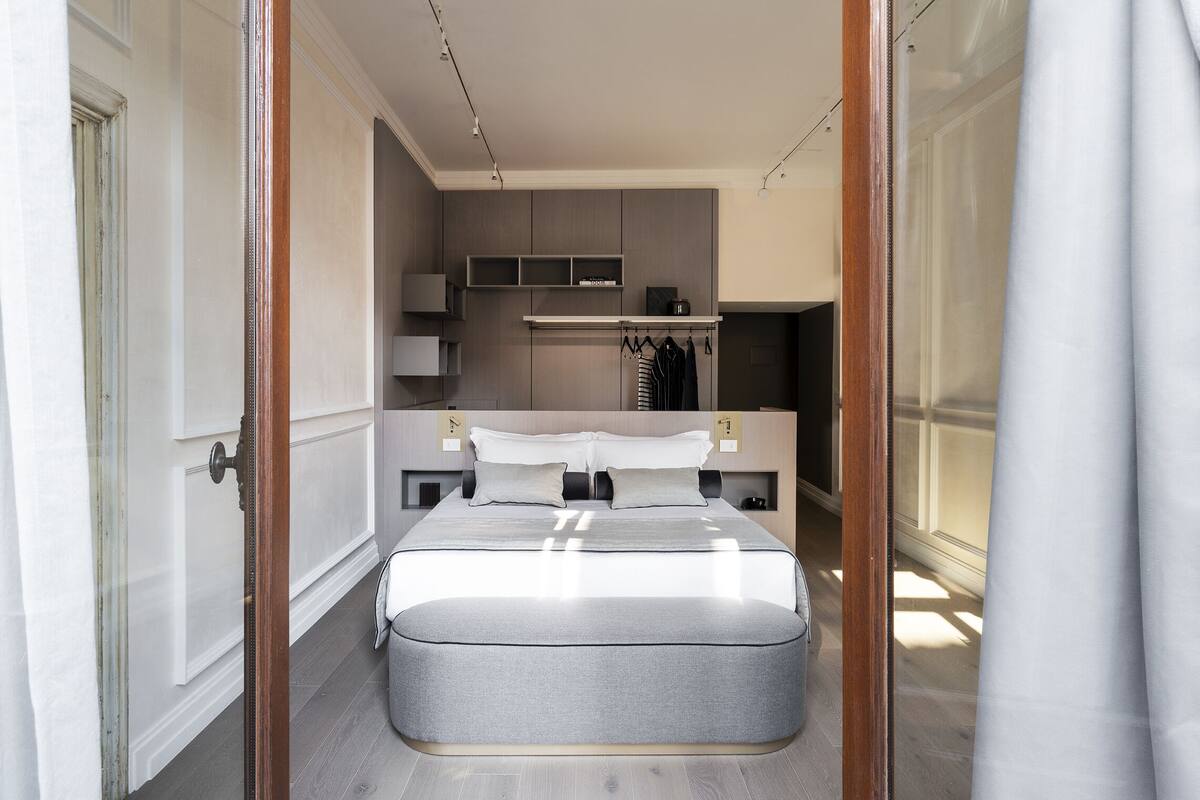 A modern bedroom with a large bed, bedside tables, a wardrobe, and a built-in shelf unit.