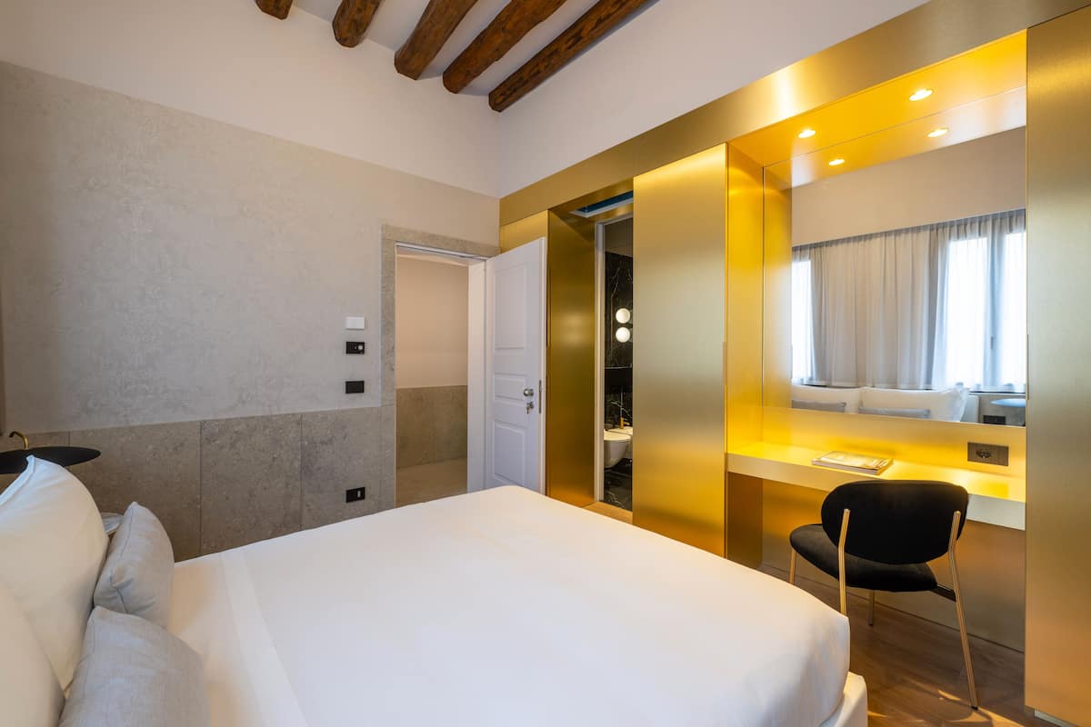 A hotel room with a large bed, a desk with a chair, a bathroom, and a mirror.